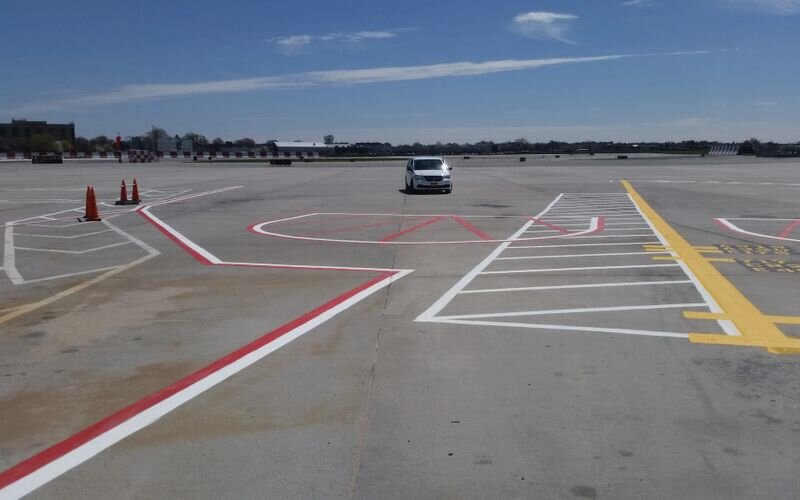 A car is driving through an intersection in the middle of a parking lot.