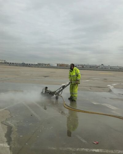 A man in yellow jacket standing on beach next to fire hose.