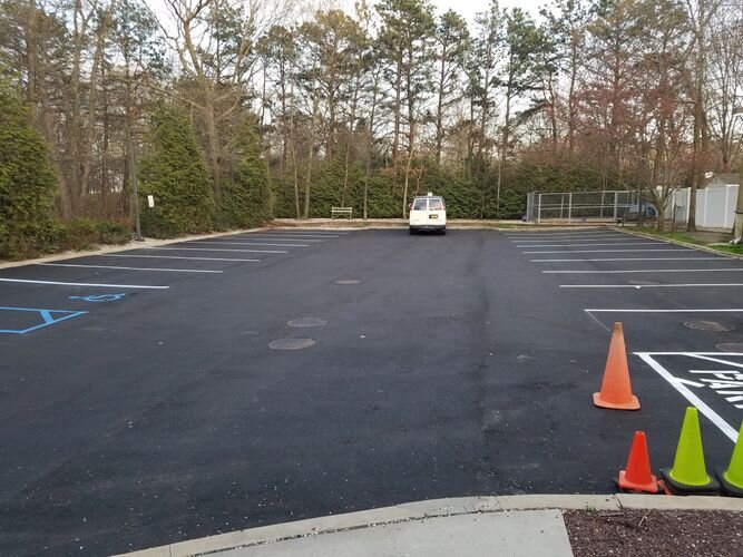 A white van driving down the street in an empty parking lot.