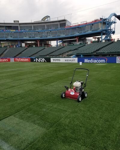 A red lawn mower on the grass in front of an empty stadium.